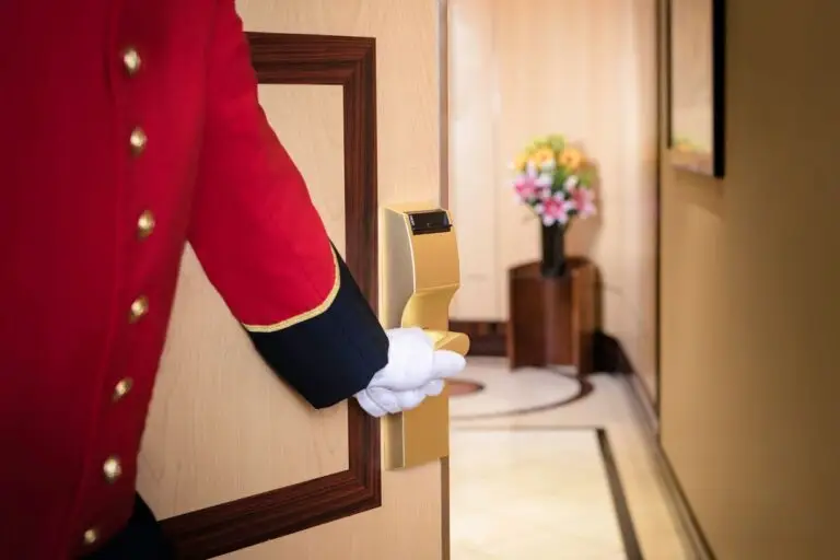 A bellhop dressed in Cunard uniform welcomes guests to their suite