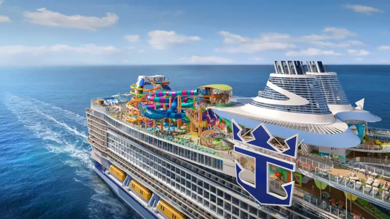 A large cruise ship, the Royal Caribbean Legend of the Seas, sails on open blue water with colourful water slides, pools, and recreational areas on its top deck under a clear sky. The Royal Caribbean logo is visible on the ship’s side.