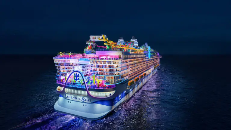 The large, brightly lit Royal Caribbean Legend of the Seas cruise ship sails at night, featuring colourful lights, outdoor decks, water slides, and multiple entertainment areas, all reflecting on the dark ocean water.